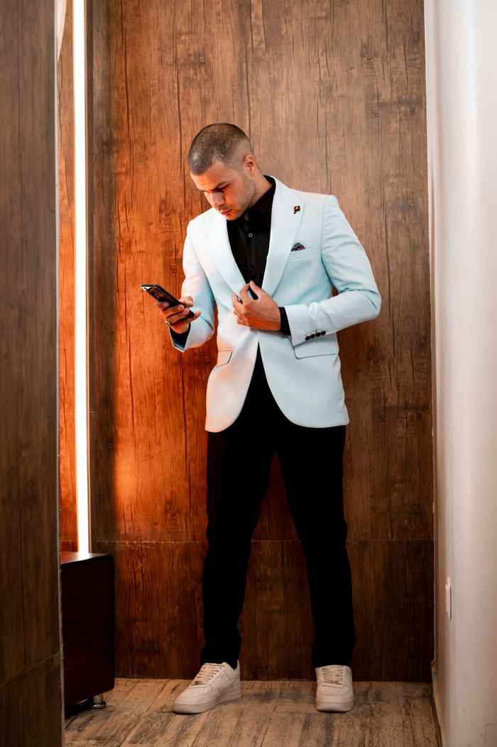 services-03 Elegant man in white blazer using smartphone in a sophisticated wood-paneled setting.