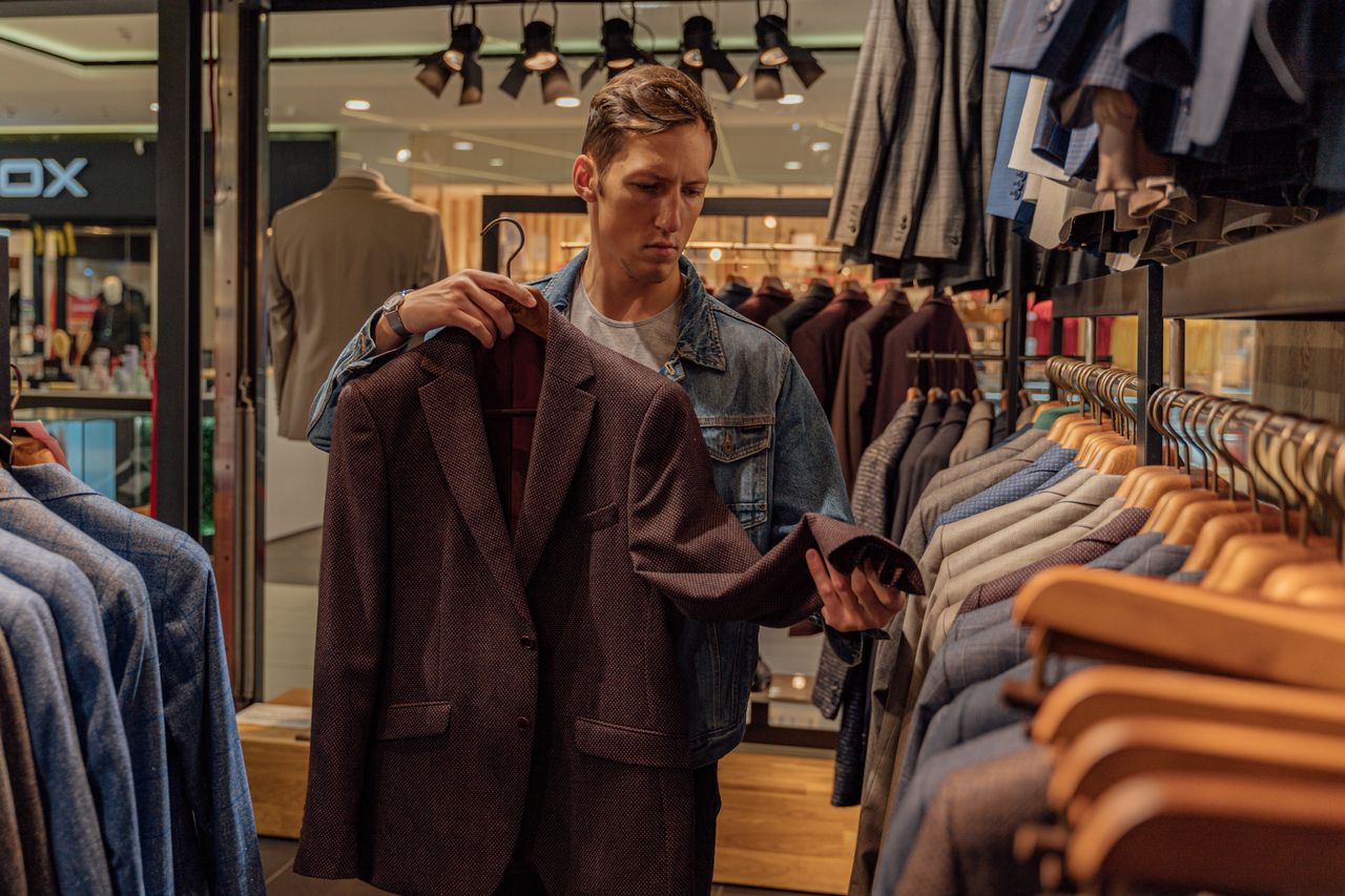services-01 Man browsing stylish blazers in a modern clothing store, considering fashion options.
